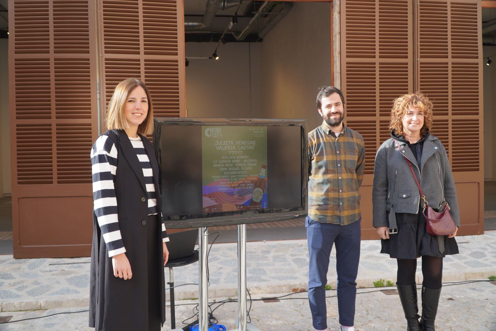 Antònia Roca, consellera de Cultura del Consell de Mallorca; Toni Jaume, organizador del Mobofest; y Xisca Mora, alcaldesa de Porreres, posan junto al cartel del Mobofest 2024.