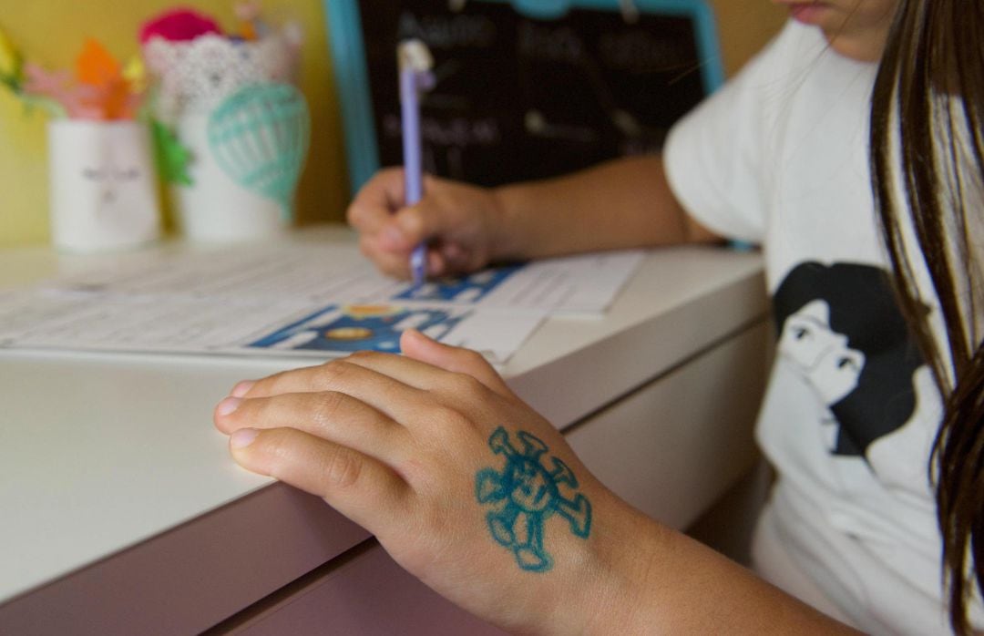 Una niña hace deberes del colegio con un dibujo del coronavirus en el dorso de la mano. 