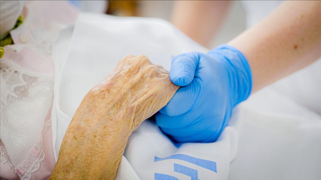 Una profesional sanitaria da la mano a una paciente en el hospital. 
 