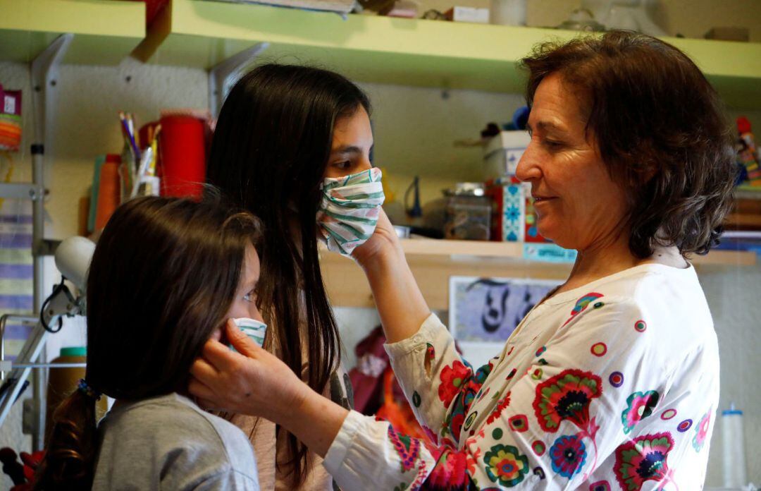 Una mujer prueba a dos niñas una mascarillas para que puedan utilizarlas a partir del próximo lunes 27, tras el anuncio del Gobierno de que los menores de catorce años podrán acompañar a un adulto en las actividades que ya permite el estado de alarma, como ir al supermercado, a la farmacia o al banco.