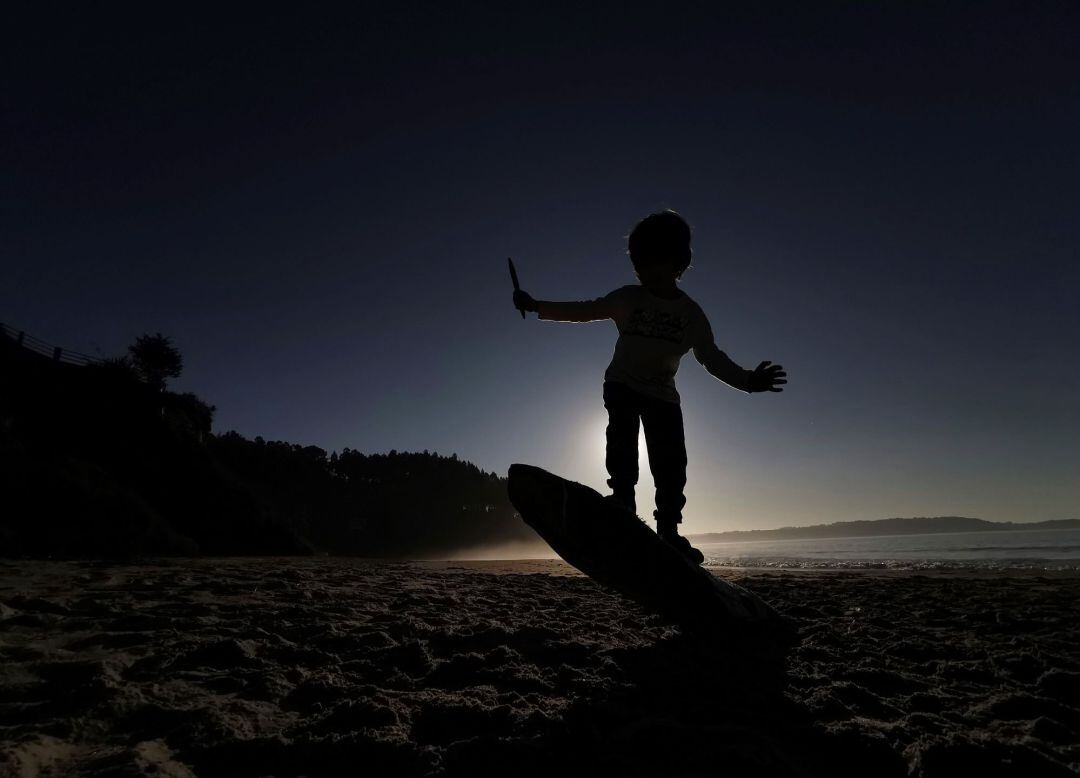 Un niño hace equilibrios sobre el tronco de un árbol arrastrado por el mar a una playa, en una imagen de archivo