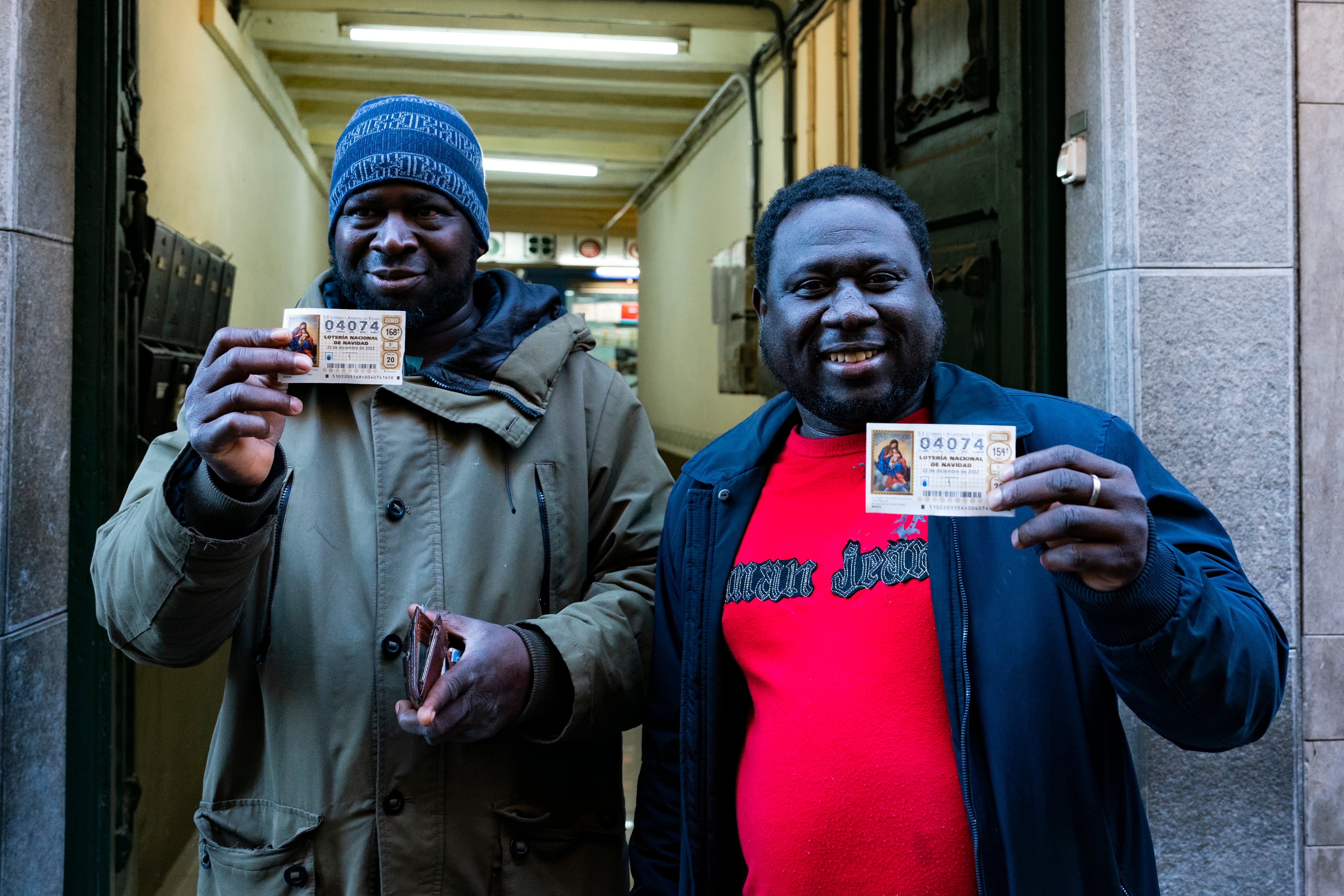 Ibrahim y su amigo, gambianos residentes en la población de Olot, posan frente la administración de lotería número 1 de Olot (Girona), Alfredo Alfaro, con sus respectivos décimos del número 04074, agraciado con el segundo premio.