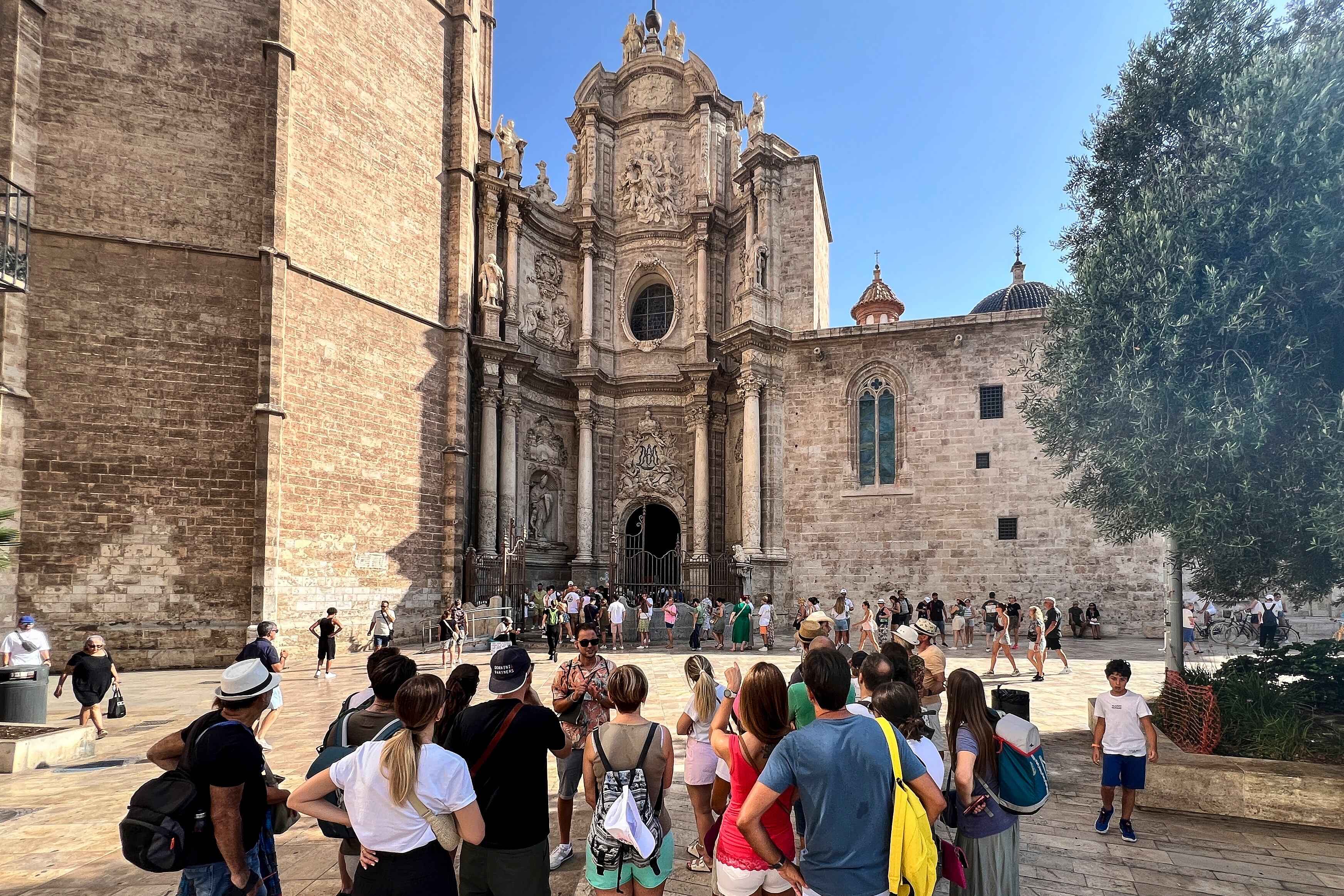 Un grupo de turistas escucha las indicaciones de su guía, mientras otros hacen cola para entrar a la catedral en el centro histórico de la ciudad de València