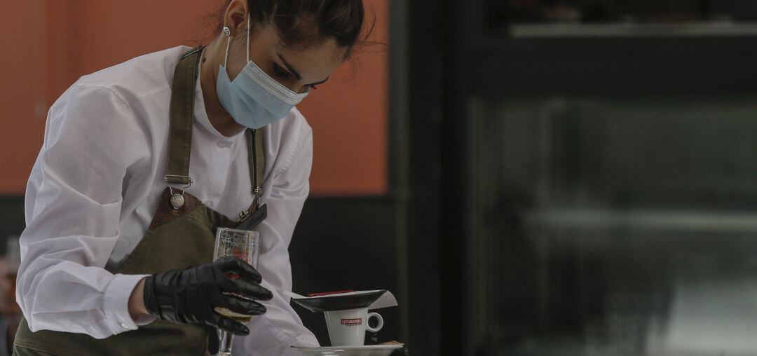 Una camarera con mascarilla y guantes atiende un bar