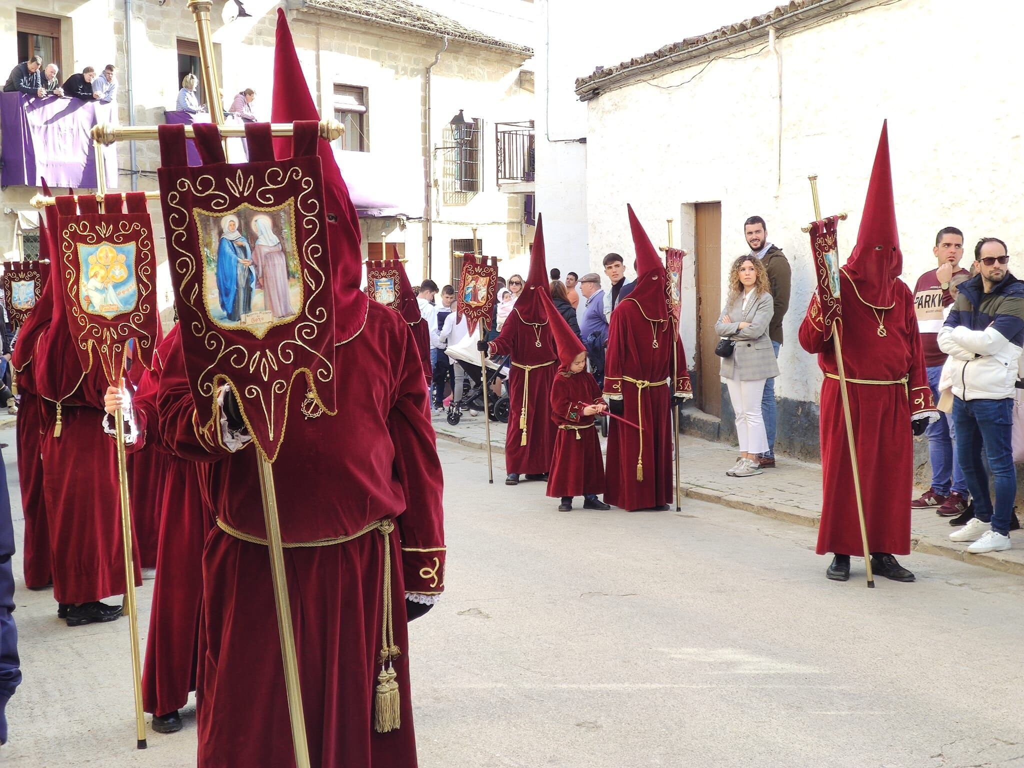 Personas contemplan el paso de nazarenos de Semana Santa durante una procesión en Baeza