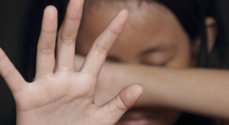 Imagen de una niña tapándose la cara con un brazo y con la mano.