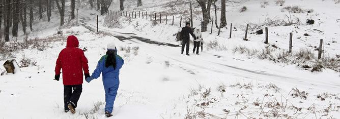 Dos parejas pasean por el alto de Ibañeta donde se acumulaban cerca de tres centimetros de espesor de nieve tras las borrascas que han caracterizado la jornada de este lunes.