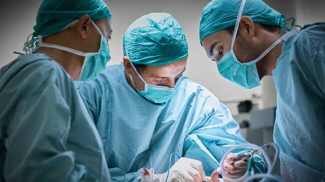 Plastic surgeons operating patient for breast implant. Team of doctors are in scrubs at operating room. They are at hospital.