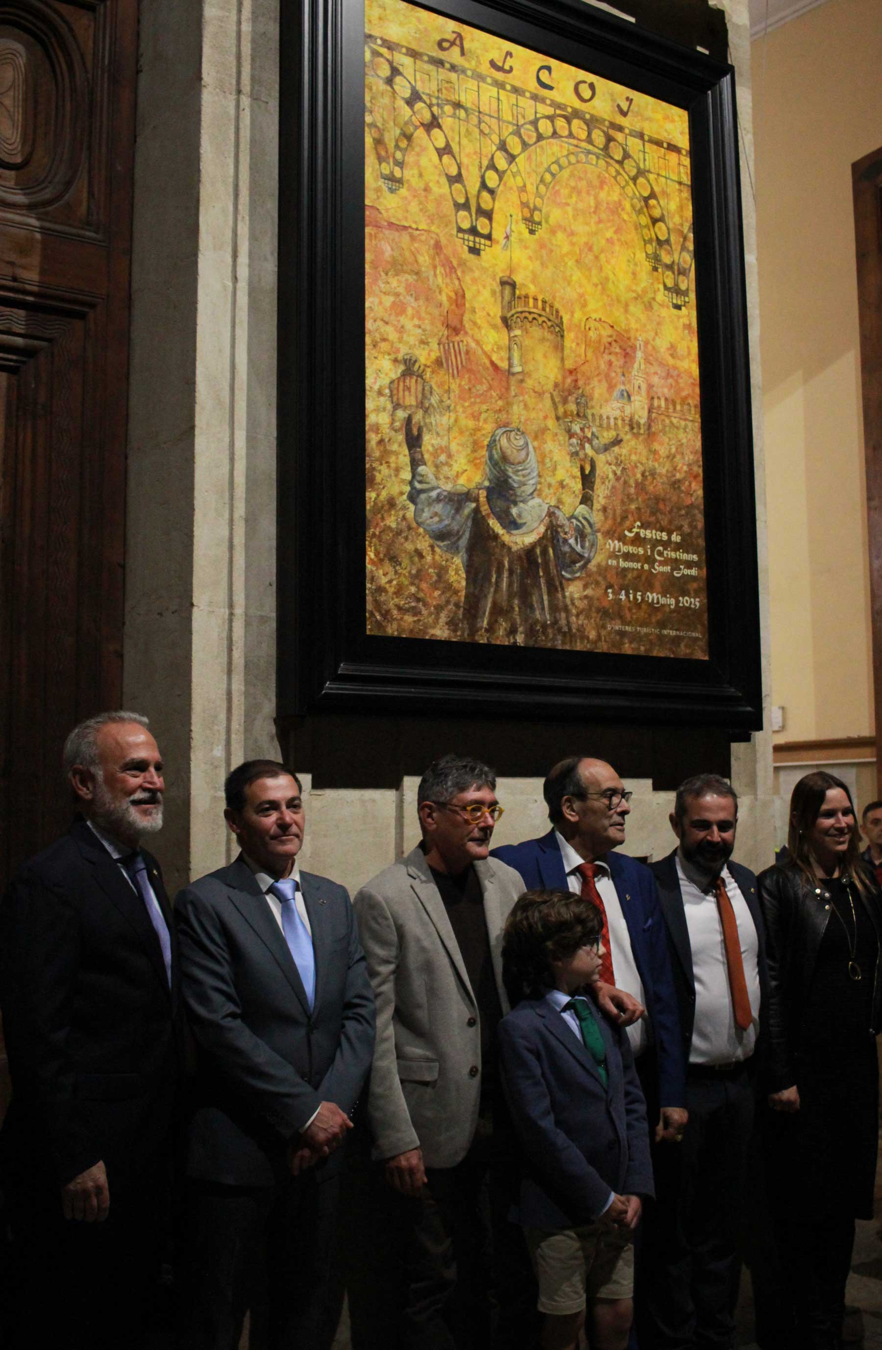 Canet junto a los cargos del 2025, capitanes, alféreces y el Sant Jordiet, justo bajo del cartel anunciador de las Fiestas de este año