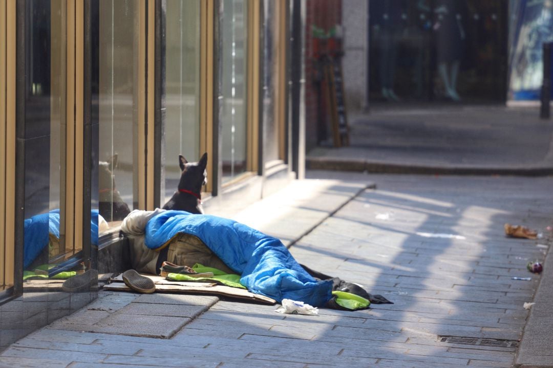 Una persona mendiga en la calle con su perro