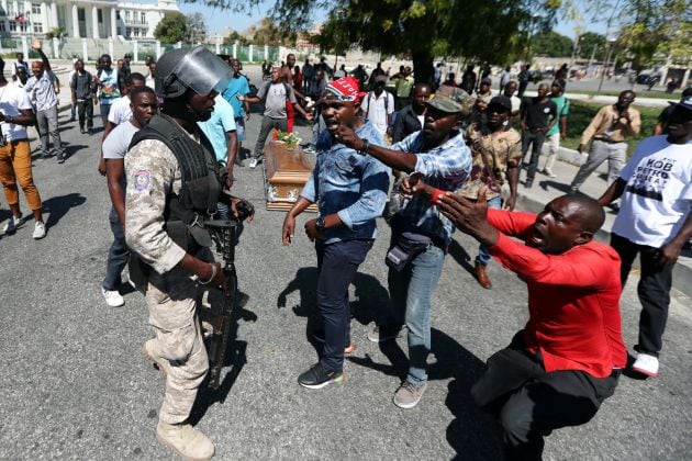 Local residents argue with a policeman while the casket of a man shot dead during anti-government protests lies on the ground in Port-au-Prince, Haiti, February 22, 2019