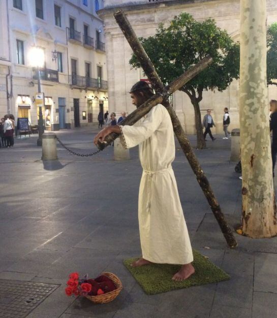 Un nazareno con la cruz al hombro puede verse en estos días por las calles de Sevilla