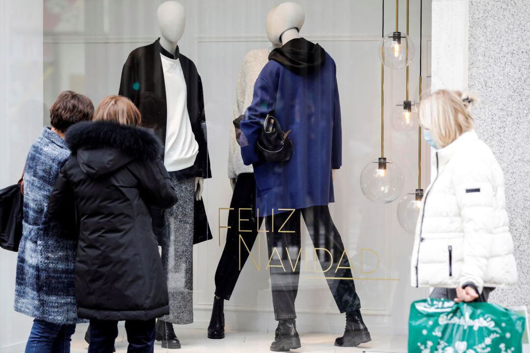 Varias personas pasan por el escaparate de un comercio.