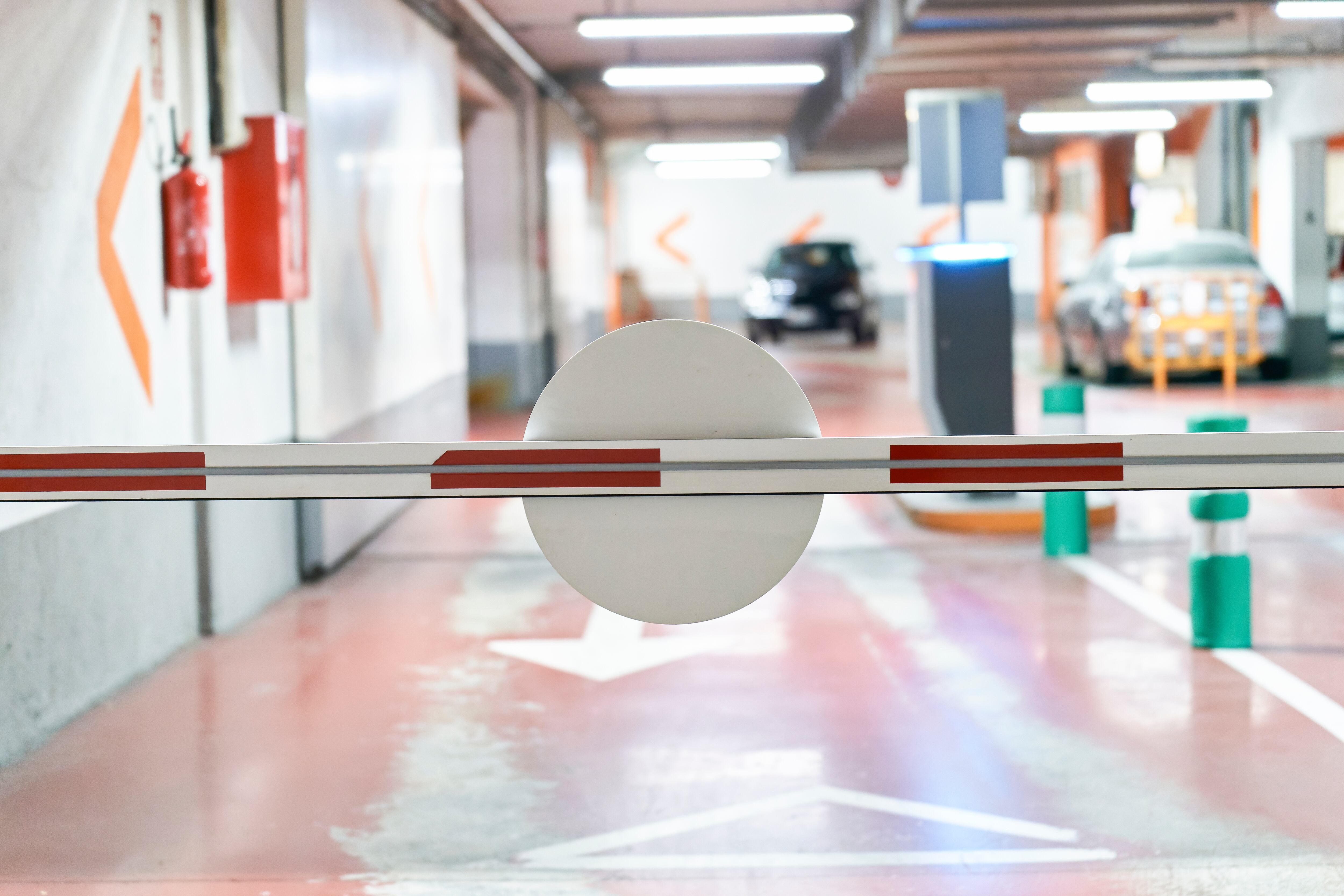 automatic safety barrier with stop sign in a parking lot inside a building, rear view with cars in the background