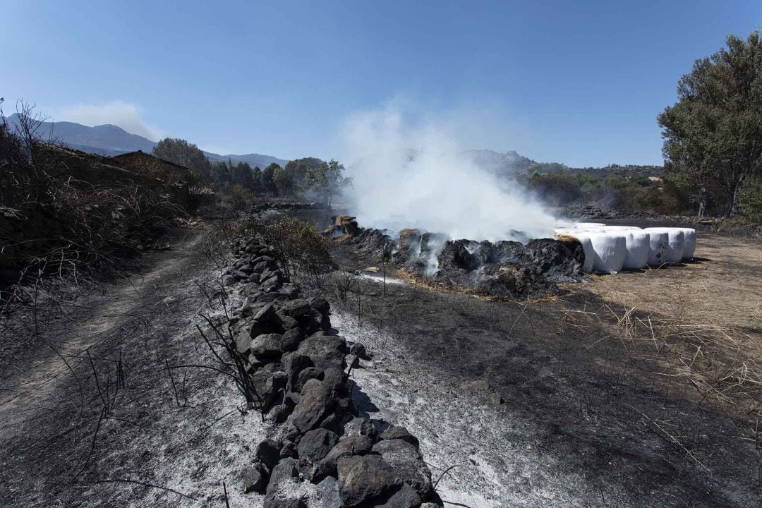 Pacas de paja ardiendo junto a una casa