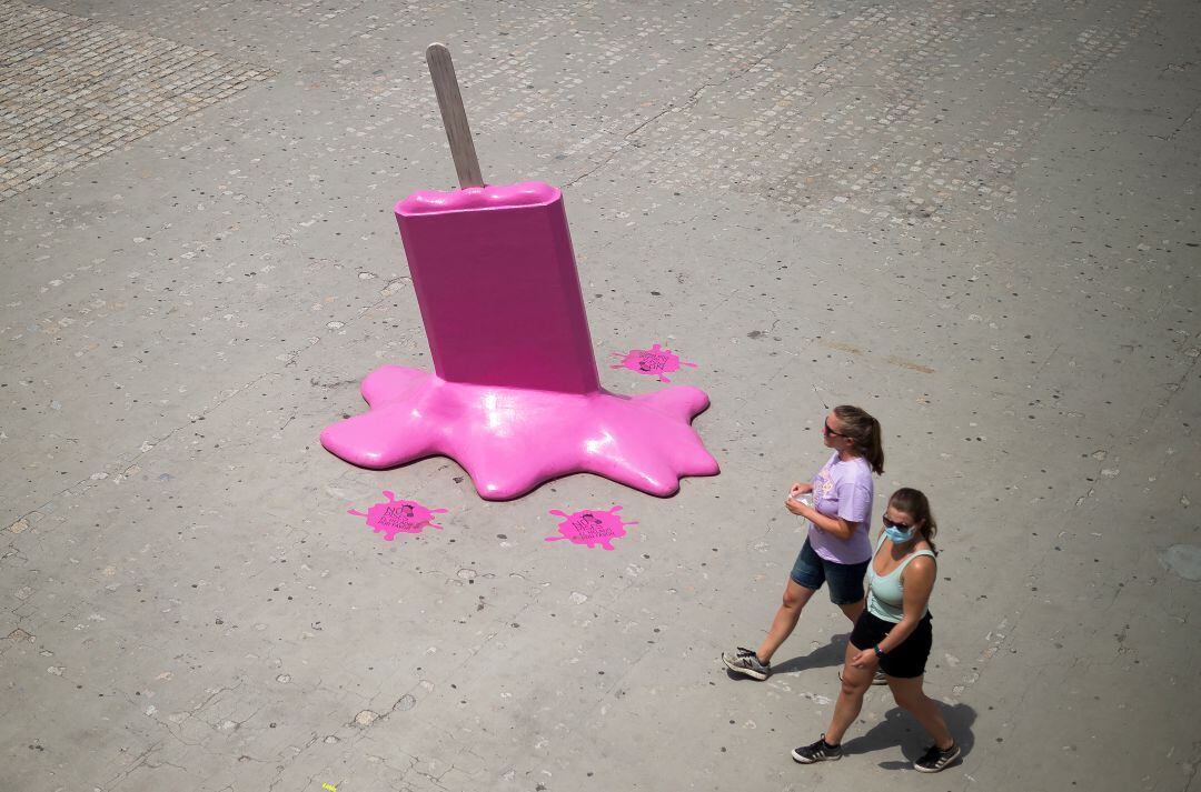 Dos mujeres pasan junto a una escultura de helado en el paseo &#039;Muelle Uno&#039; (Málaga) durante un caluroso día de verano en medio de la pandemia de coronavirus