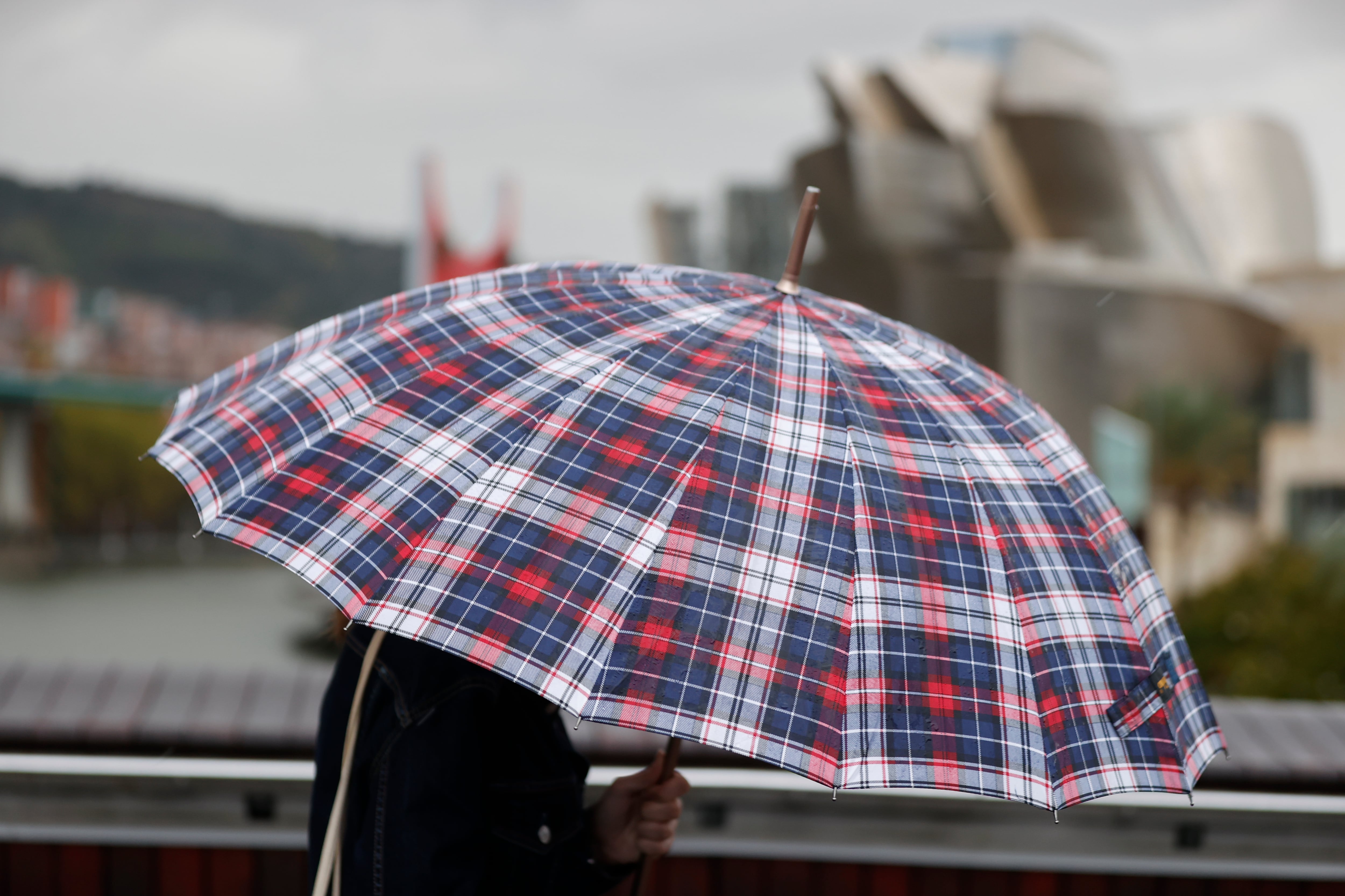 Un persona se protege con un paraguas de la lluvia este viernes en Bilbao, como consecuencia de la borrasca Aline con lluvias, fuerte viento y mar arbolada en la consta. EFE/Luis Tejido