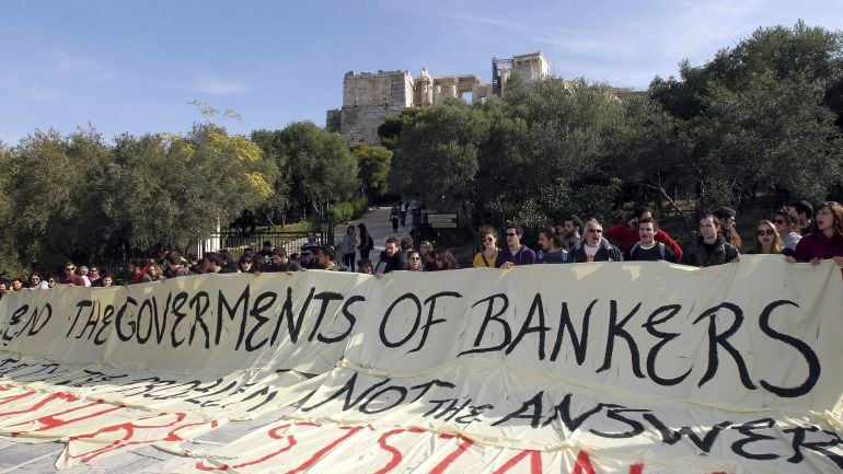 Manifestantes y afiliados a la Coalición de Izquierda radical (SYRIZA) sostienen una pancarta en la que se lee &quot;Acabemos con el gobierno de los bancos. La austeridad es el problema, no la respuesta&quot; durante una protesta en la entrada de la Avcrópolis en A