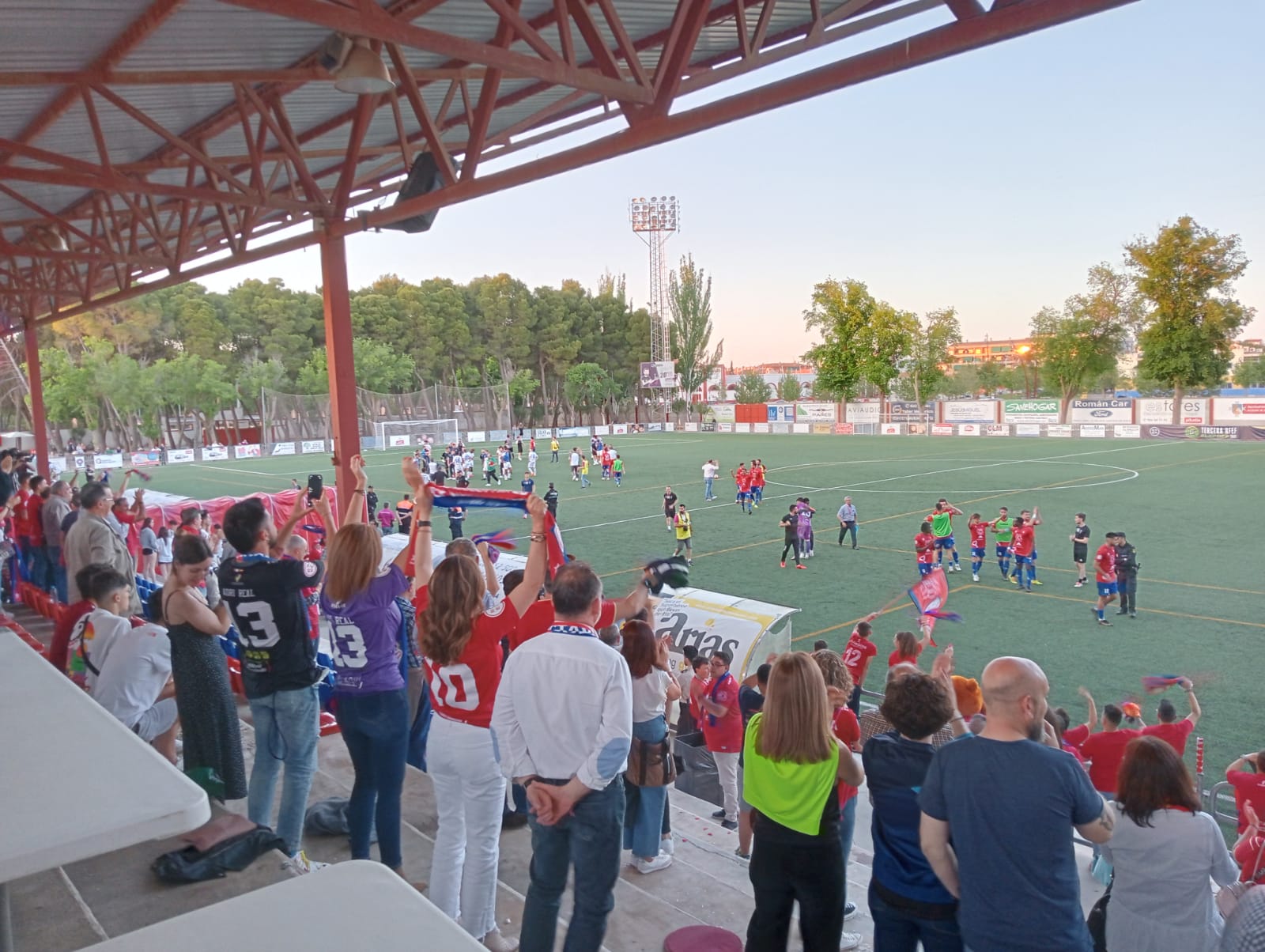 Aficionados del Villarrobledo celebran el triunfo, al fondo jugadores del Illescas