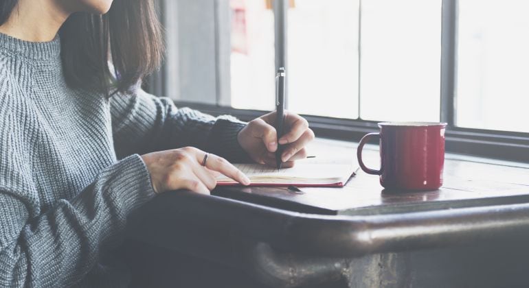 Imagen de una chica escribiendo junto a un ventanal. 