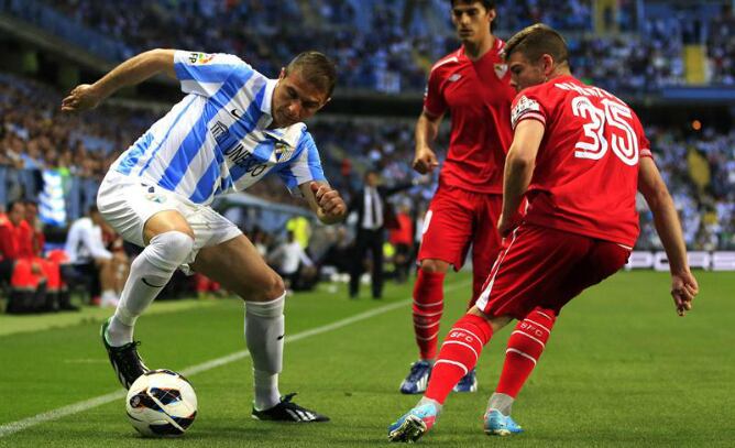 El centrocampista del Málaga Joaquín Sánchez trata de escapar entre los sevillistas Alberto Moreno y Diego Perotti durante el partido de Liga que han disputado los dos equipos andaluces en La Rosaleda.