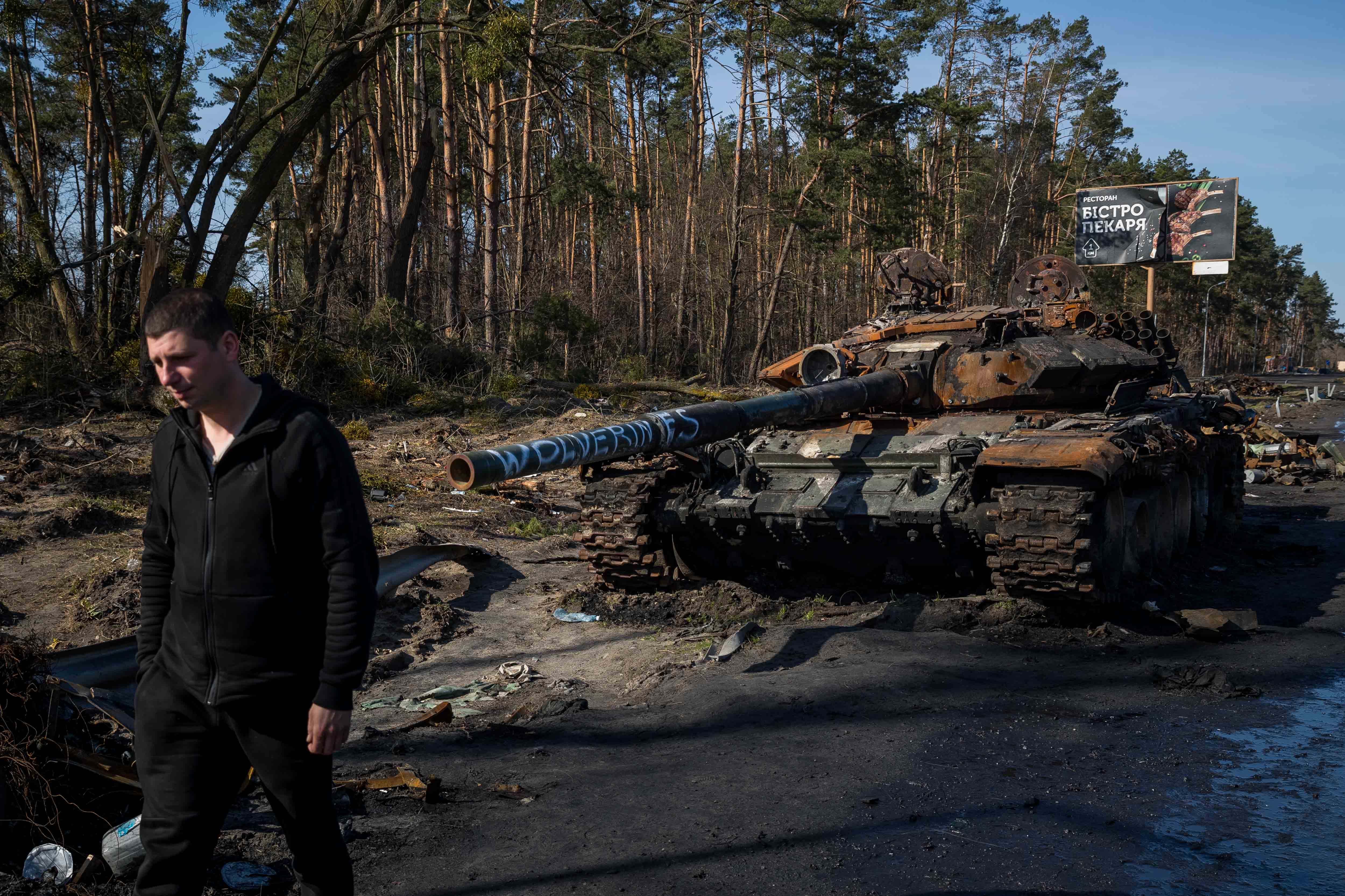 Sasha camina delante de un tanque ruso destruido, el 11 de abril del 2022, en Irpin (Ucrania). La carretera que conduce a las ciudades recientemente liberadas al oeste de Kiev está repleta de tanques rusos destrozados que ahora reposan en la cuneta formando una hilera infinita.